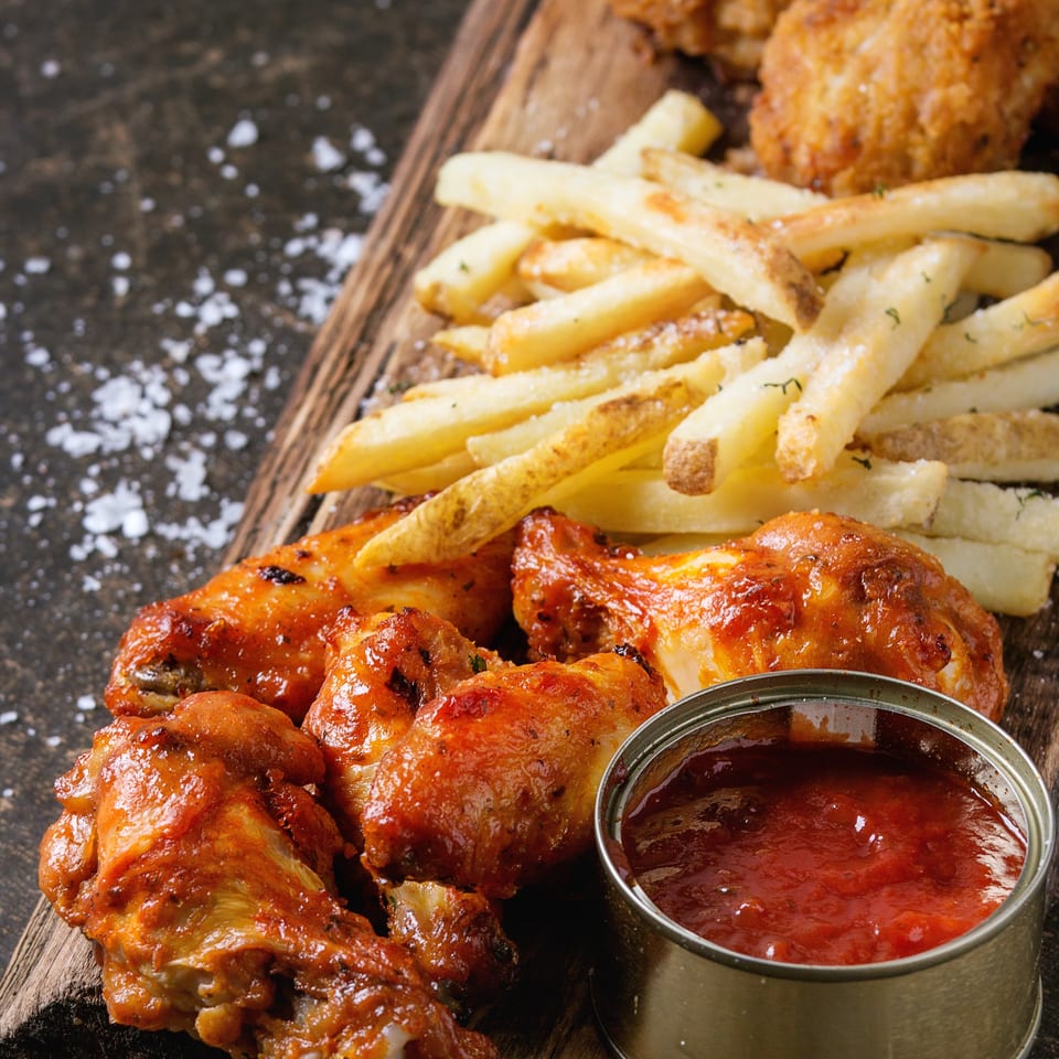 Spicy chicken wings, crispy french fries, and a side of red dipping sauce on a wooden board.