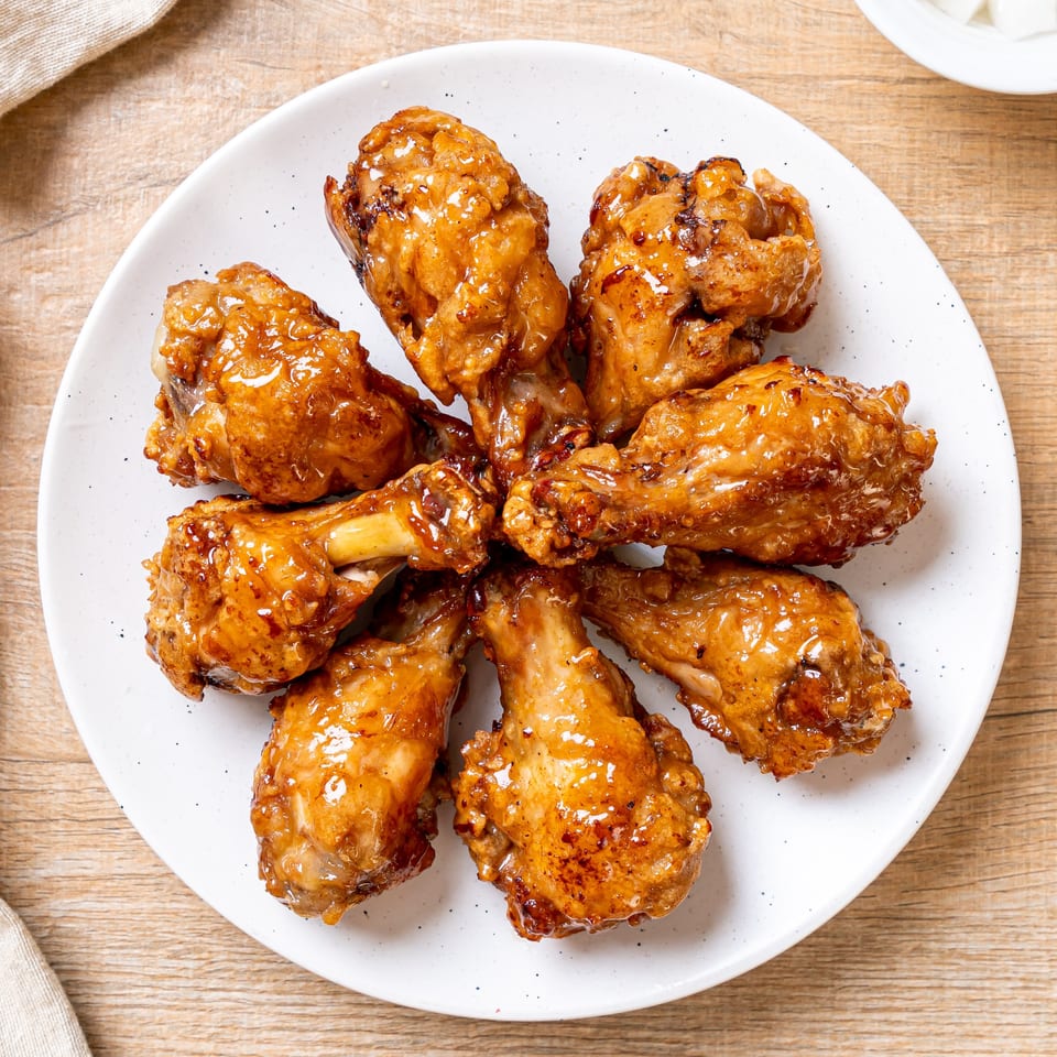 A white plate holds eight golden-brown, glazed chicken drumettes and wings on a wooden table.