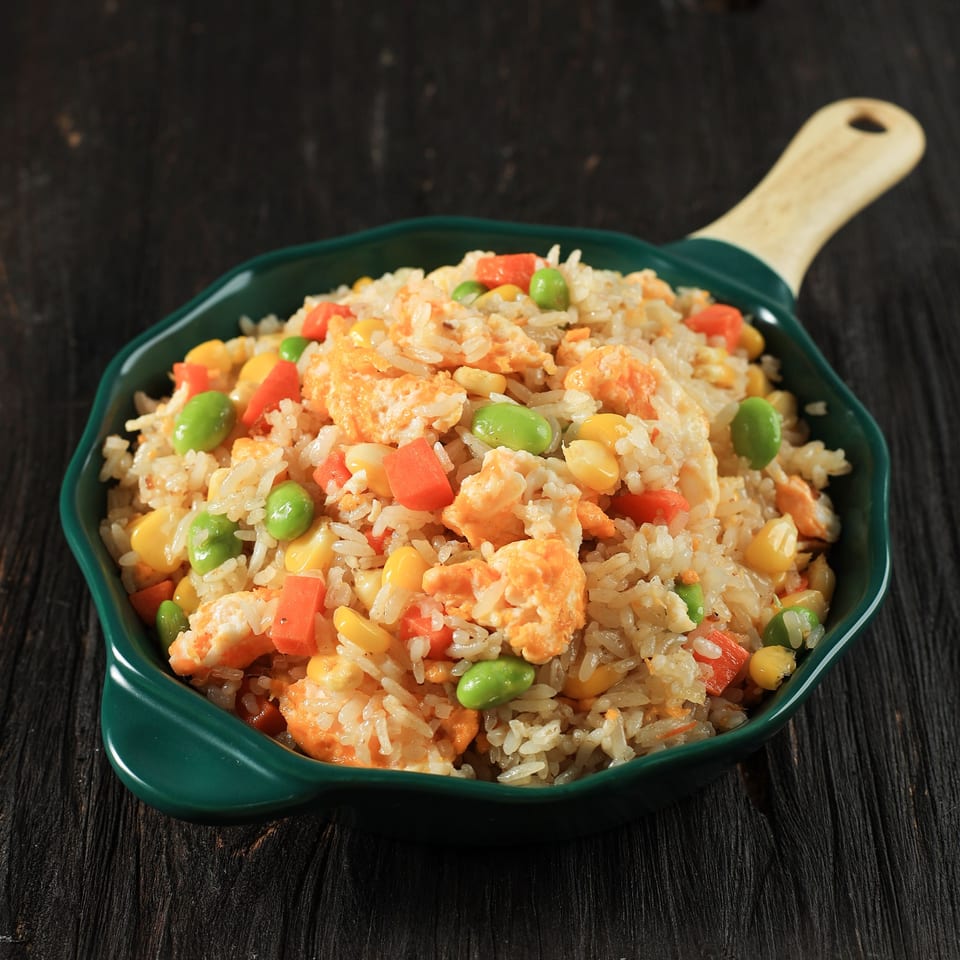 Fried rice with scrambled egg, carrots, corn, and edamame in a green skillet.