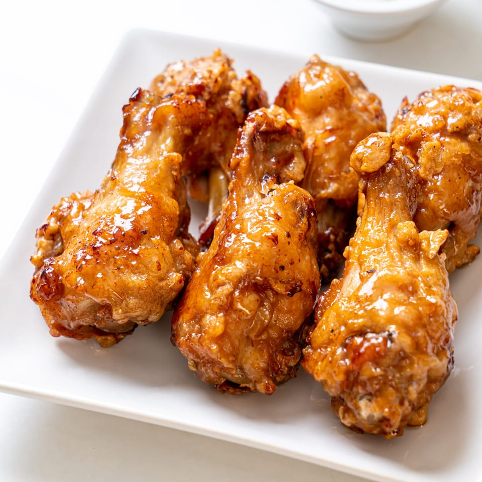 A white rectangular plate holds several golden-brown, glazed chicken drumsticks, ready to be served.